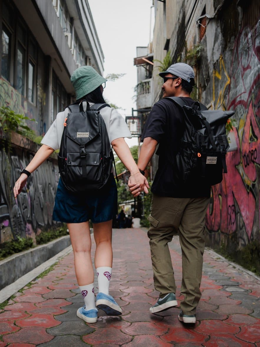 Two people in SIDSNEAKS walking hand in hand down a graffiti alley