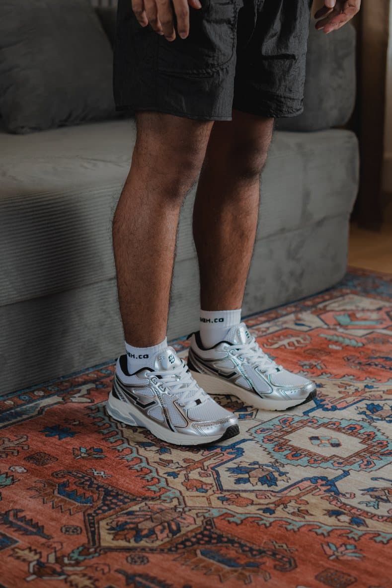 Silver SIDSNEAKS runners worn with white socks on a patterned rug
