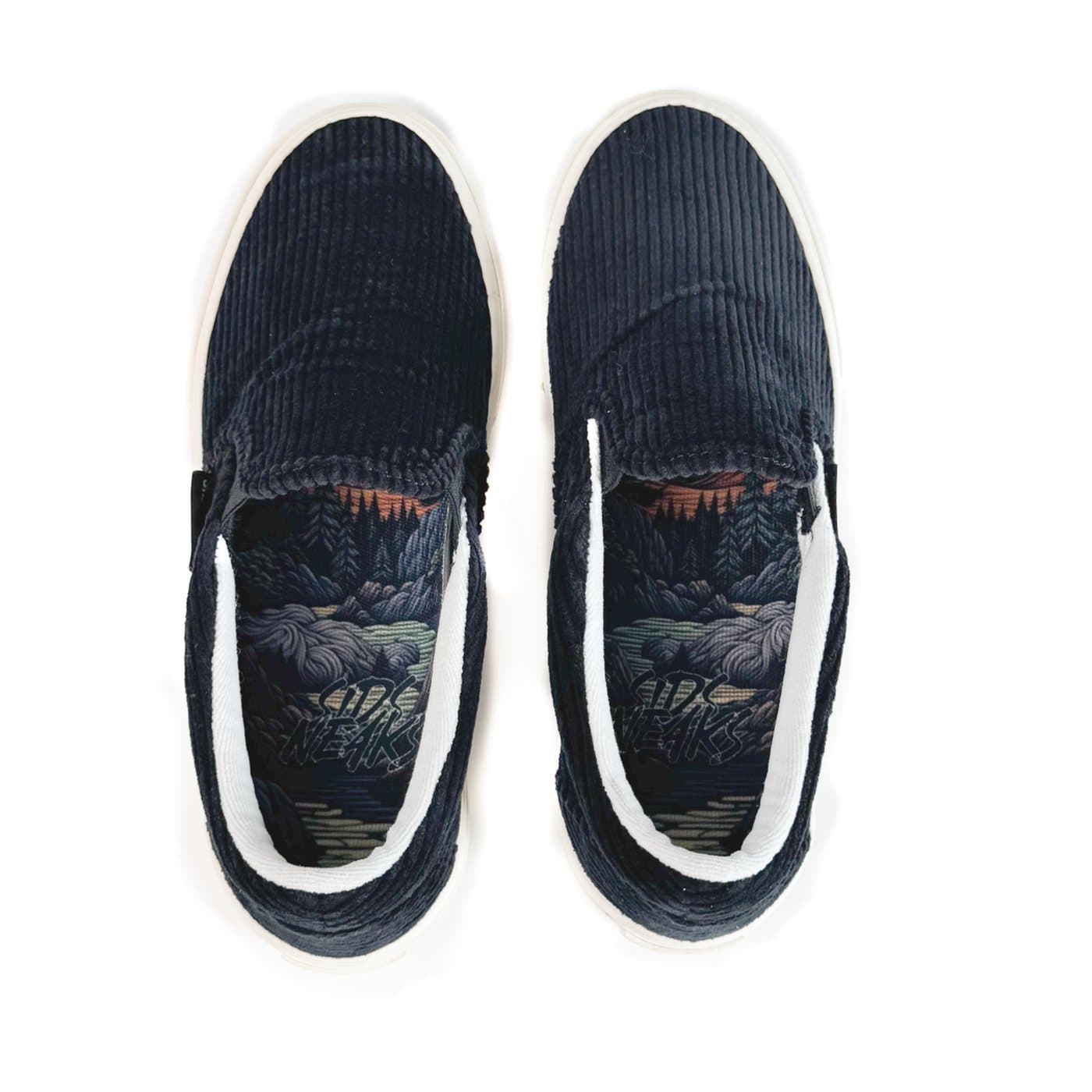 Top-down view of black corduroy slip-ons showing the illustrated landscape insole